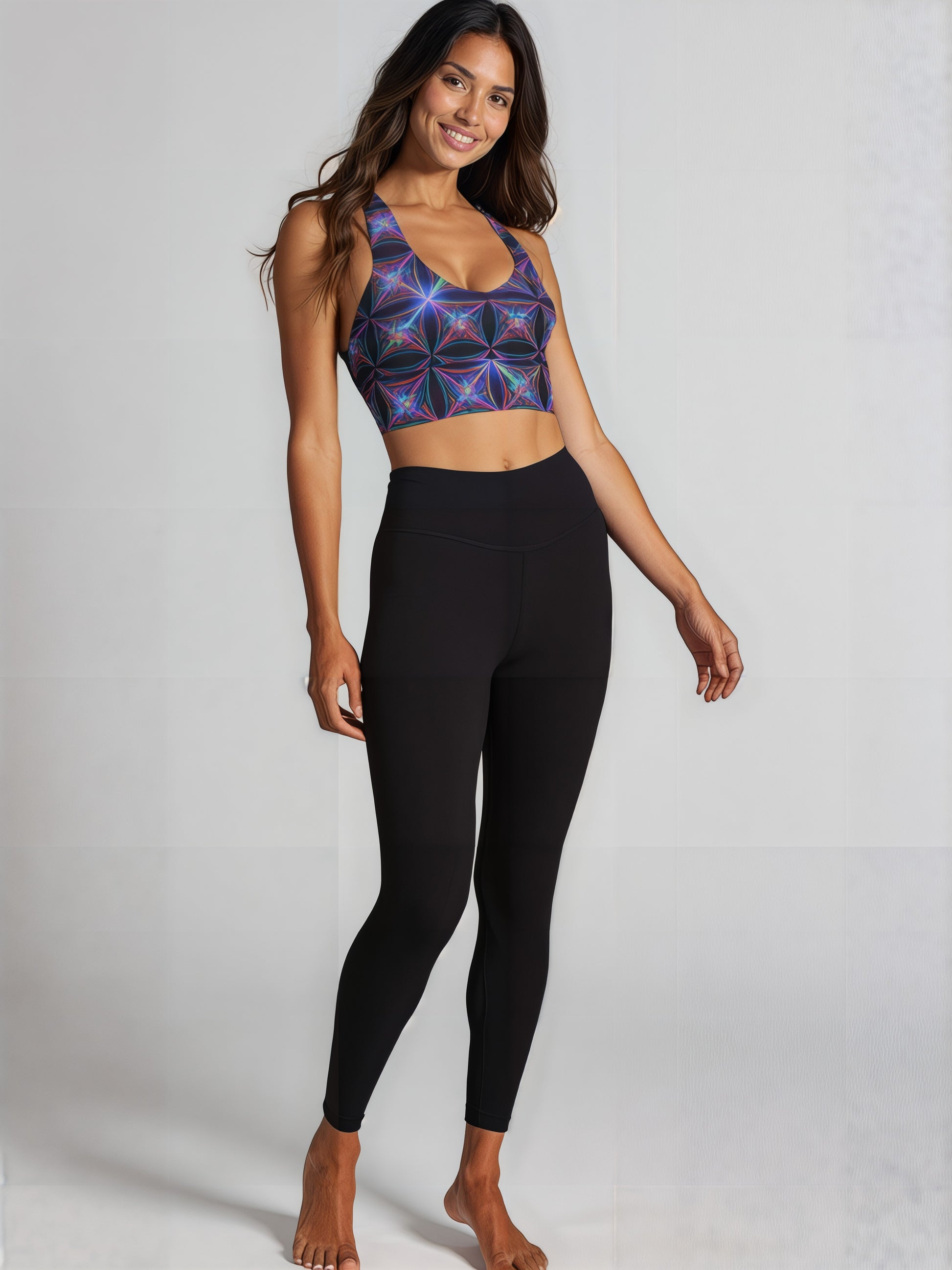 Woman wearing Blue Voltage longline sports bra with a vibrant blue and purple geometric pattern, smiling with arms raised against a plain background