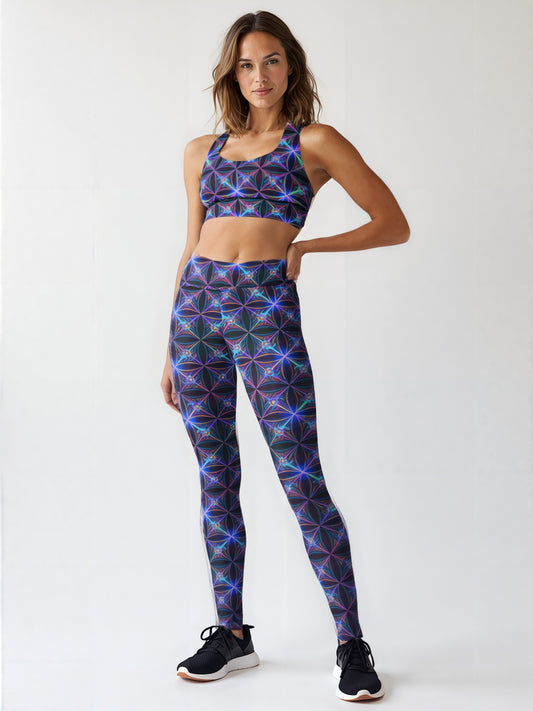 Woman wearing Blue Voltage Yoga leggings and a matching sports bra featuring a vibrant electric blue and purple geometric pattern, standing in athletic sneakers against a light background.