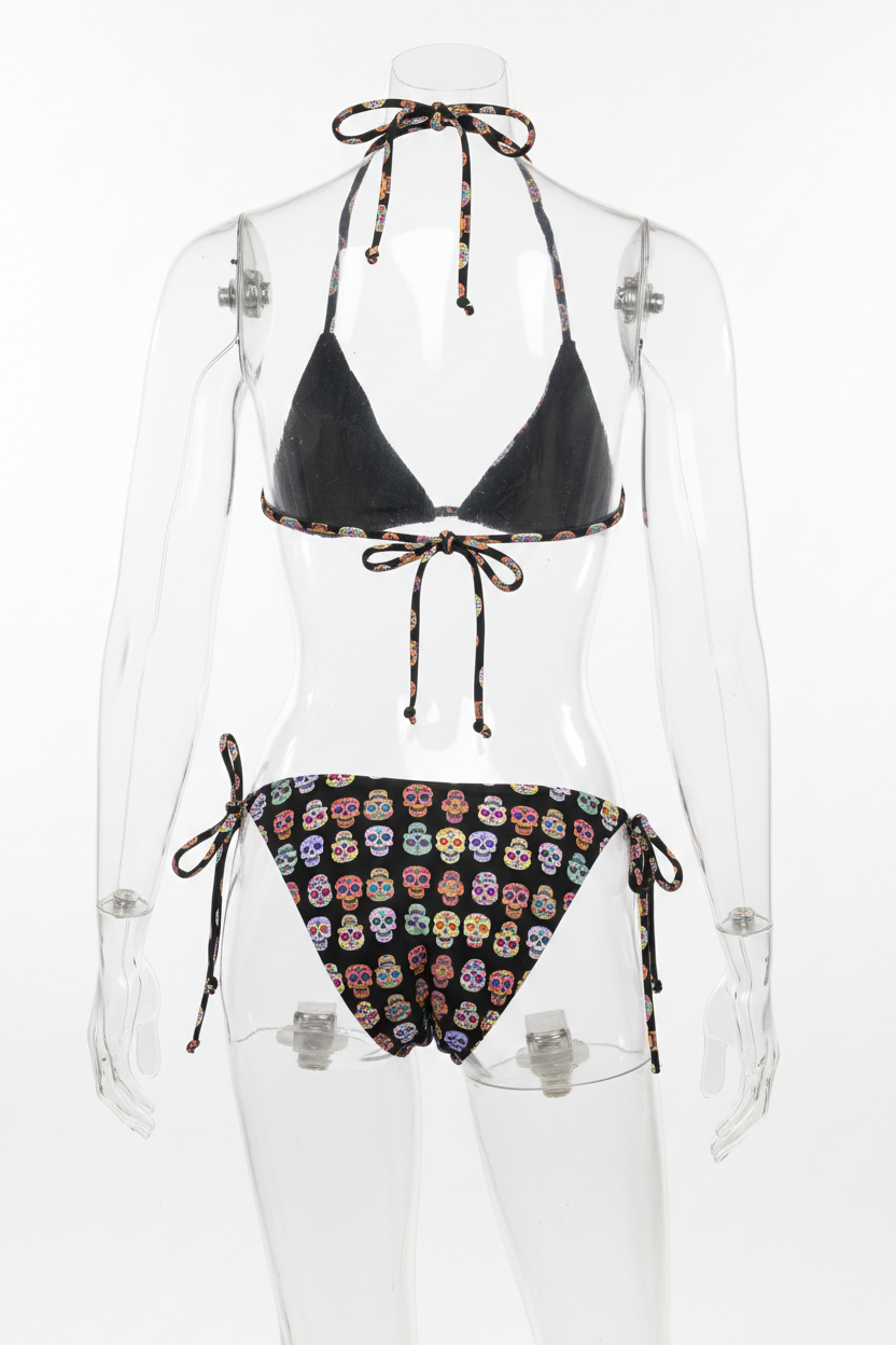 A two-piece string bikini set on a plain white background. The top is solid black with patterned tie straps, and the bottom is black with a colorful sugar skull print.