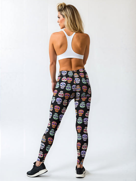 Back view of a woman wearing black leggings with a colourful sugar skull pattern, paired with a white racerback sports bra and black sneakers, standing against a plain background.