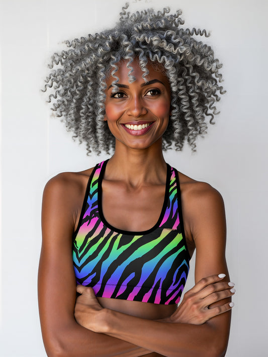 Woman wearing Technicolour Essential Active Bra with bold neon green, blue, and pink zebra stripes, smiling and standing against a plain background