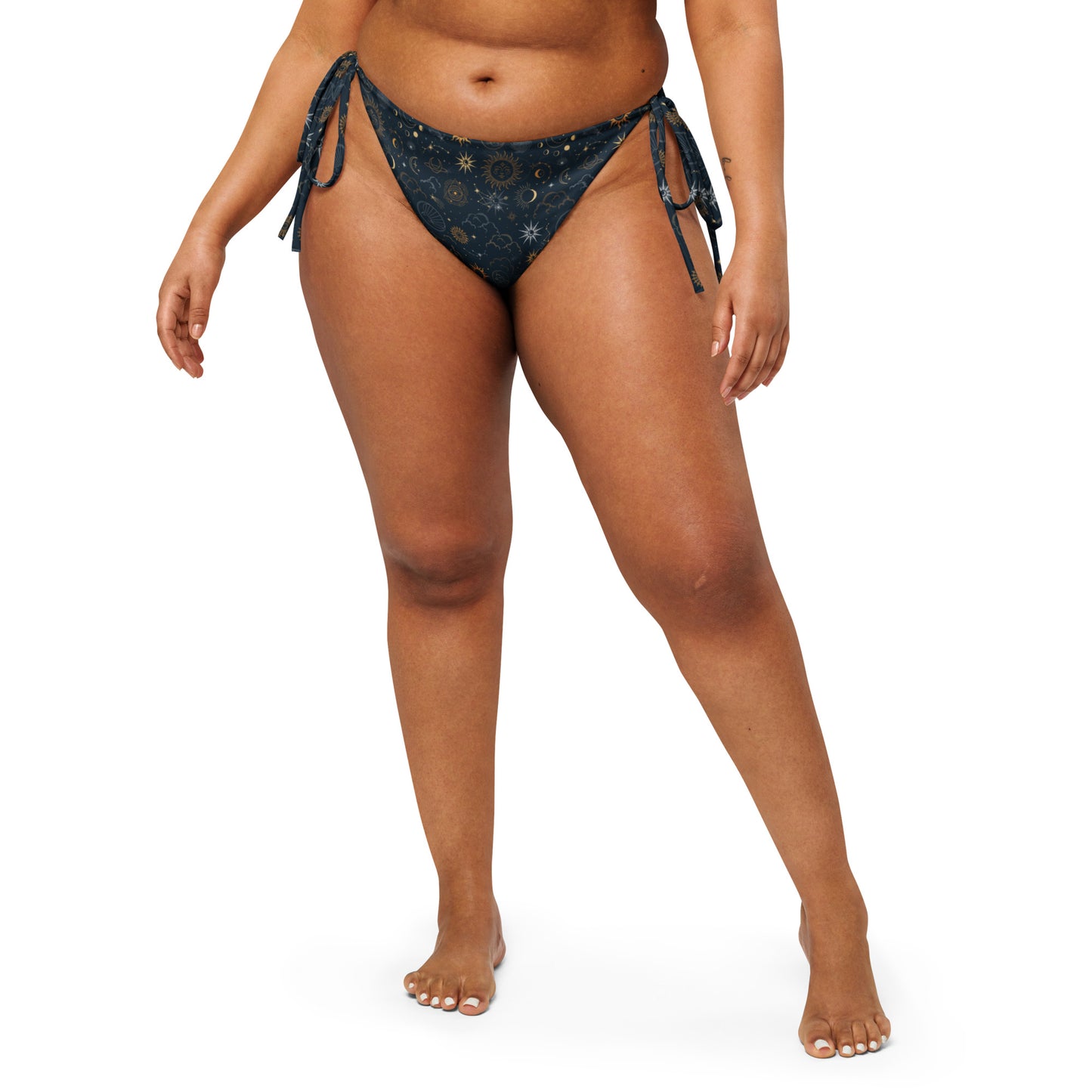 Celestial Luxe string bikini bottom with gold sun, moon, and star celestial print on a dark background.