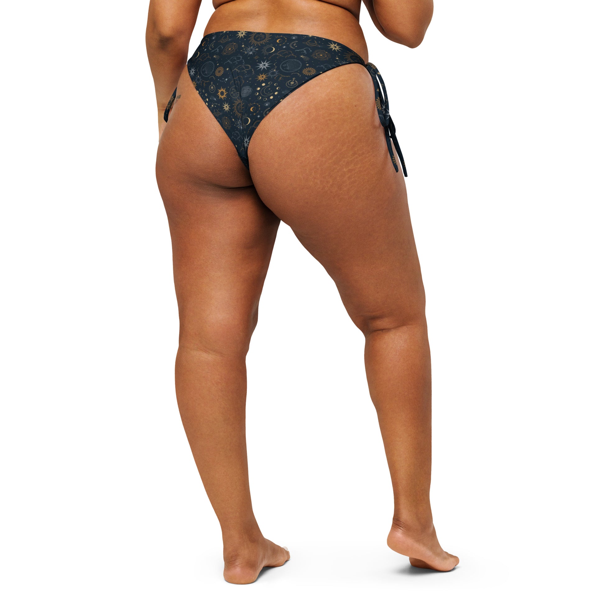 Celestial Luxe string bikini bottom with gold sun, moon, and star celestial print on a dark background.
