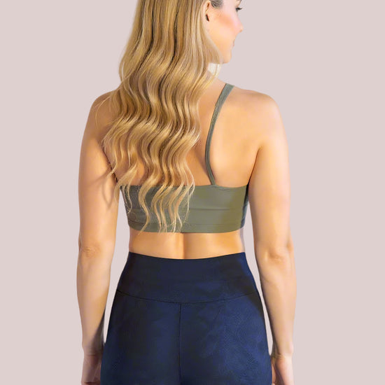 A woman with long, wavy blonde hair is shown from the back, wearing an olive green sports bra and high-waisted, dark navy Shadowleaf Yoga shorts with subtle textured detailing, standing against a light background.