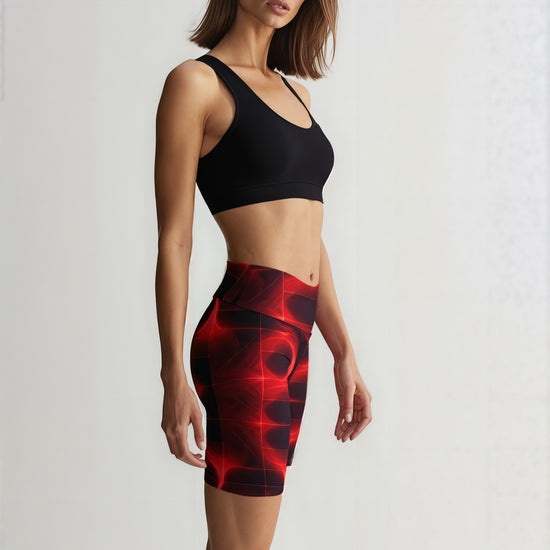 Side view of a woman wearing Blaze Ignite Yoga Shorts with a vivid red and black abstract pattern, paired with a black sports bra, standing against a plain background.