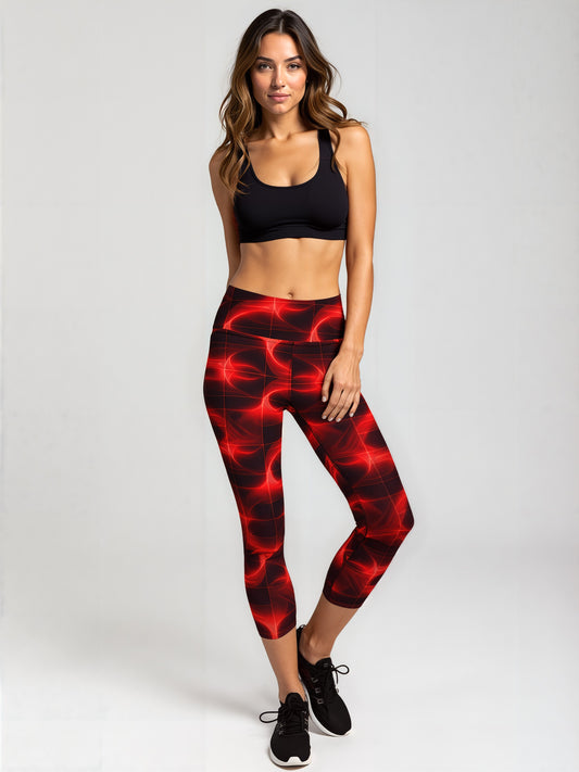 A woman stands confidently wearing Blaze Ignite Capris leggings featuring a bold, glowing red and black abstract pattern. She pairs the high-waisted, fitted capris with a simple black sports bra and black running shoes, set against a plain light background.