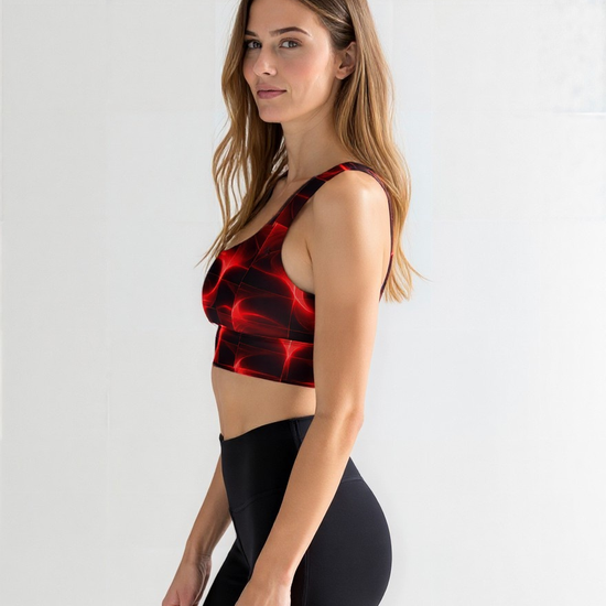 Woman wearing a Blaze Ignite longline sports bra with a vibrant red and black abstract pattern, paired with high-waisted black leggings, standing in a relaxed side pose against a plain light background.