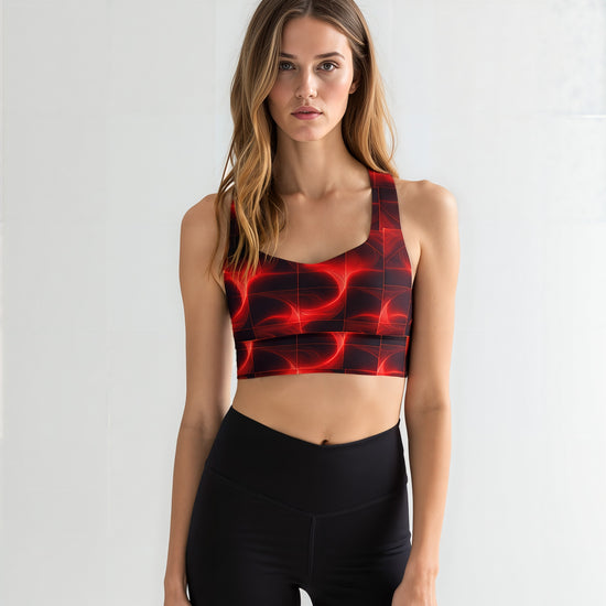 Woman wearing a Blaze Ignite longline sports bra with a bold red and black abstract pattern, paired with high-waisted black leggings, standing against a plain light background.