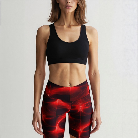Front view of a woman wearing Blaze Ignite Yoga Shorts with a striking red and black abstract pattern, paired with a black sports bra, standing against a plain background.