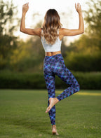 Woman in blue patterned leggings and white crop top standing on one leg in a grassy outdoor setting.