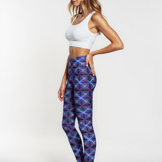 Side view of a woman wearing Blue Voltage Crossover leggings with a vibrant electric blue and purple geometric pattern, paired with a white sports bra, standing barefoot against a plain white background.