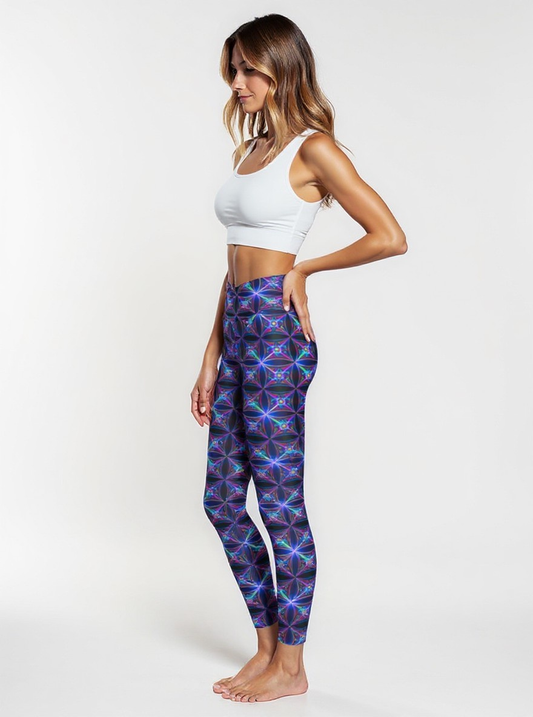 Side view of a woman wearing Blue Voltage Crossover leggings with a vibrant electric blue and purple geometric pattern, paired with a white sports bra, standing barefoot against a plain white background.