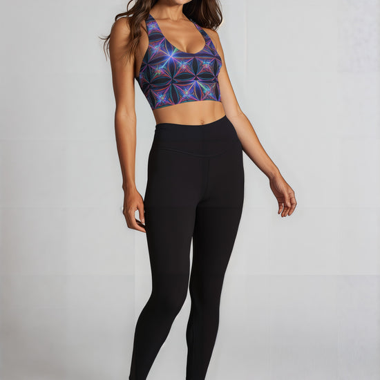 Woman wearing Blue Voltage longline sports bra with a vibrant blue and purple geometric pattern, smiling with arms raised against a plain background
