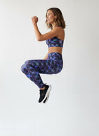 Woman in blue patterned leggings and sports bra jumping on a white background