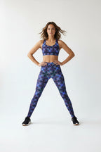 Woman in a yoga pose wearing a patterned sports bra and leggings on a white background