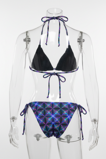 Two-piece string bikini set on a white background, featuring a solid black triangle top and matching low-rise bottoms with a vibrant purple, blue, and pink geometric flower pattern.