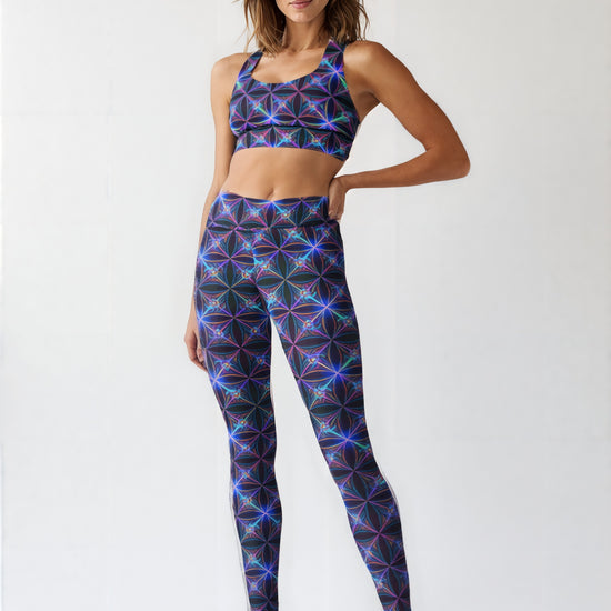 Woman wearing Blue Voltage Yoga leggings and a matching sports bra featuring a vibrant electric blue and purple geometric pattern, standing in athletic sneakers against a light background.