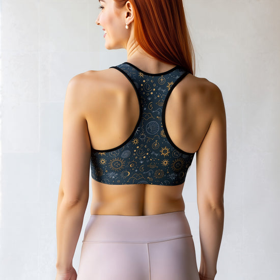 Woman shown from the back wearing the Celestial Essential Bra, featuring a dark blue fabric with a star and moon pattern, paired with light pink high-waisted leggings, standing against a light background.
