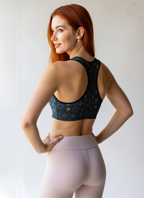 Woman shown from the back wearing the Celestial Essential Bra, featuring a dark blue fabric with a star and moon pattern, paired with light pink high-waisted leggings, standing against a light background.