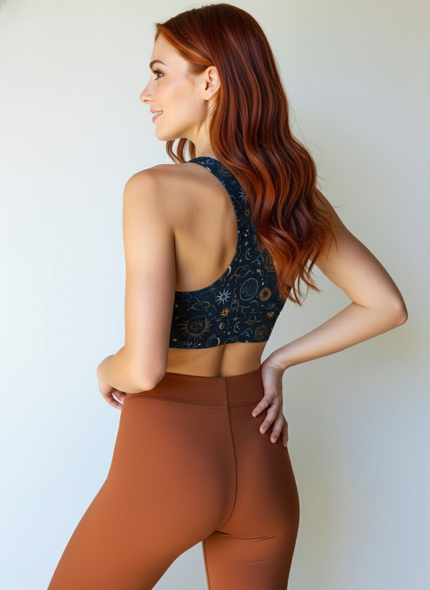 Back view of women wearing Pixie and Sherbet’s Celestial Longline Bra with a dark navy base and gold celestial sun, moon, and star print, smiling confidently against a light background.