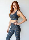 Woman wearing Pixie and Sherbet’s Celestial Longline Bra with a dark navy base and gold celestial sun, moon, and star print, smiling confidently against a light background.