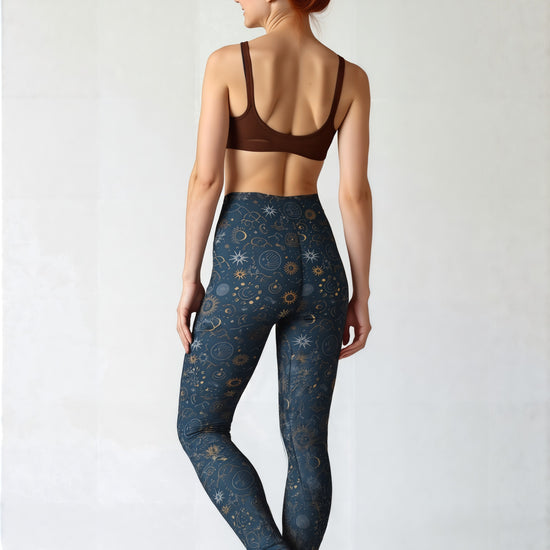 Back view of woman wearing Pixie and Sherbet’s Celestial Yoga leggings featuring a dark navy base with gold celestial sun, moon, and star print, standing barefoot and smiling in a relaxed pose against a light background.