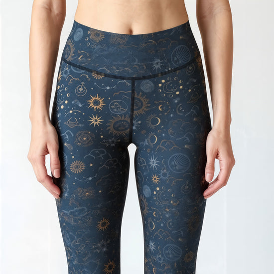 Close-up front view of a woman wearing Pixie and Sherbet’s Celestial Luxe Yoga leggings with a dark navy background and gold celestial sun, moon, and star print, highlighting the high-waisted fit and detailed pattern.