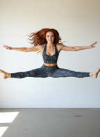 Woman in a yoga pose wearing matching blue and gold athletic outfit against a white wall.