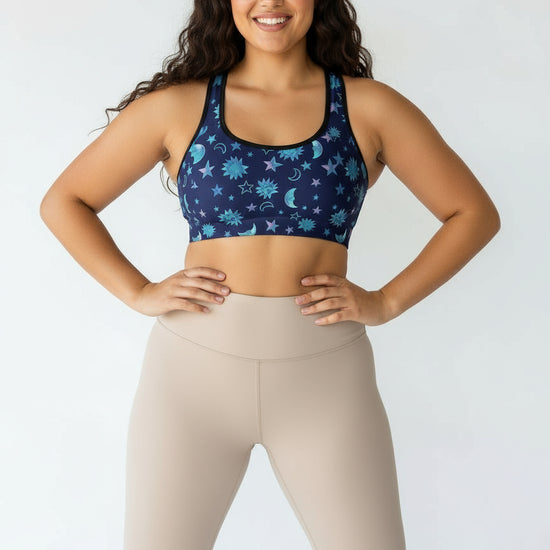 Woman wearing a blue patterned sports bra and beige leggings against a white background