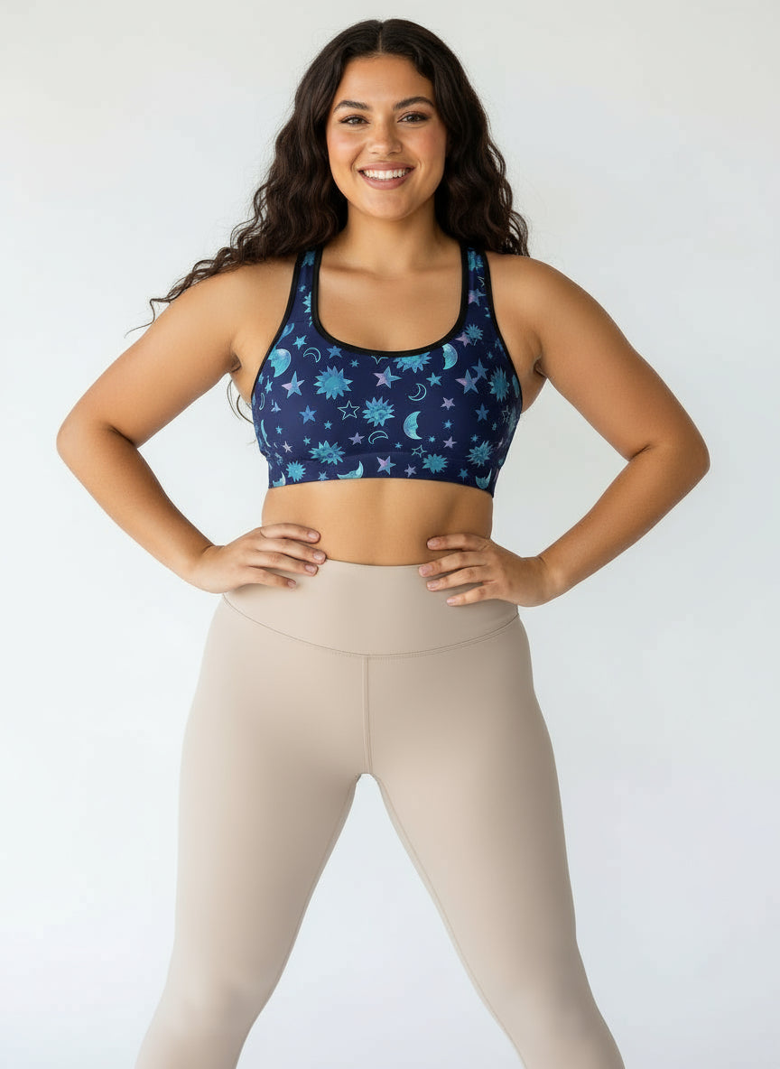 Woman wearing a blue patterned sports bra and beige leggings against a white background