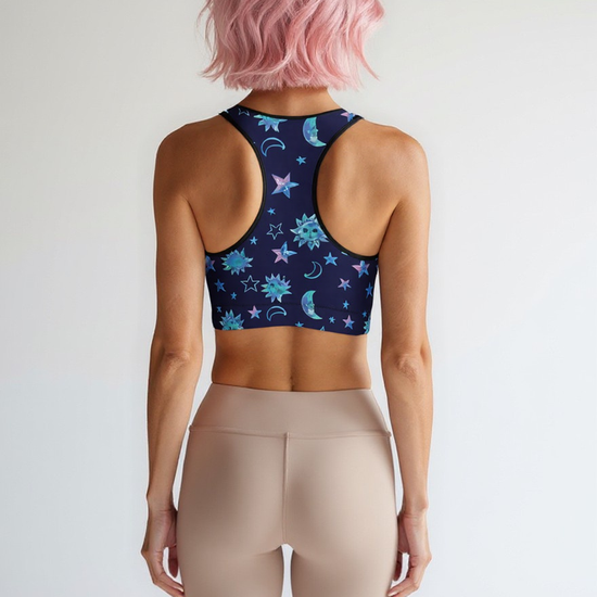 Woman showing the back of the Cosmic Calm Essential Active Bra with a navy base and pastel blue and purple celestial print, standing against a plain background