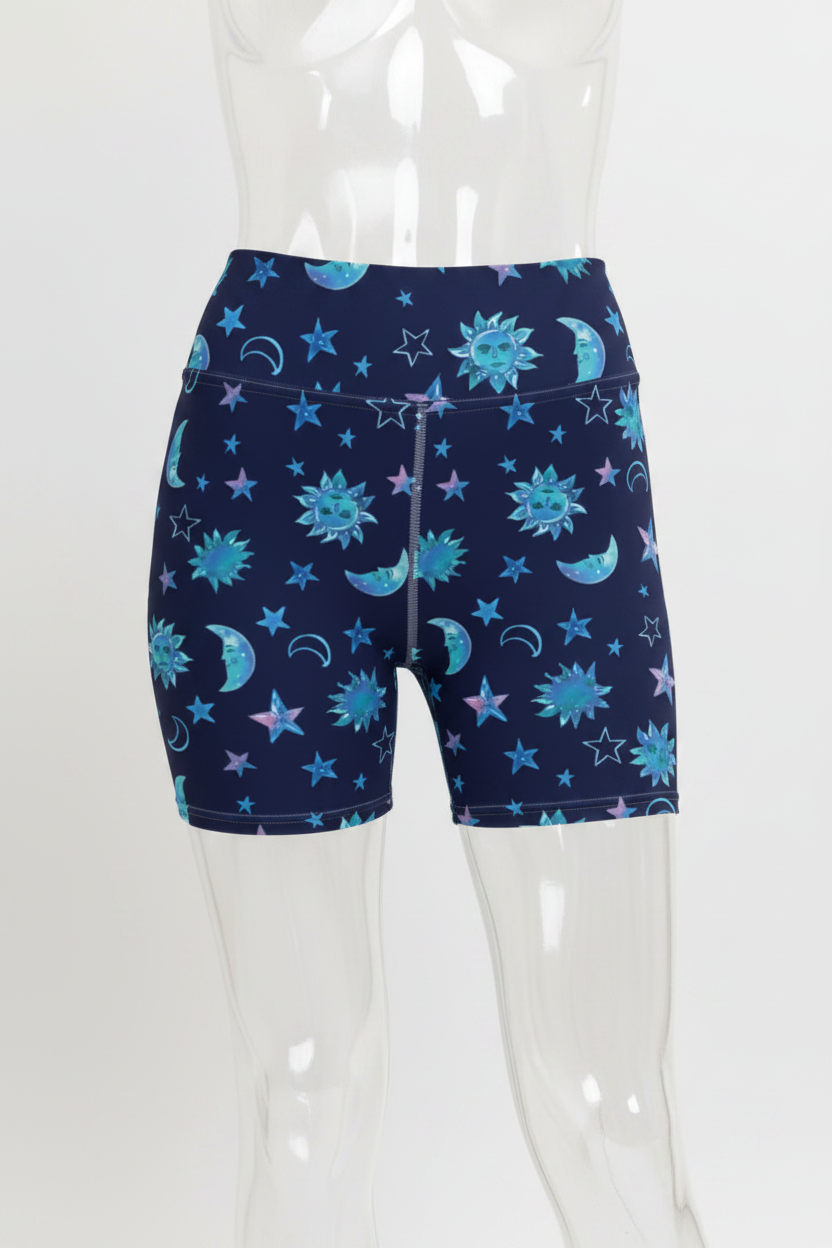 A person wearing high-waisted athletic shorts with a celestial print of stars, moons, and suns in shades of blue and teal on a dark navy background.