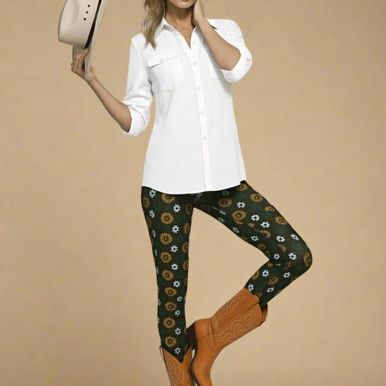 Model wearing Country Diamond Leggings with white and yellow floral print on dark green base, styled with cognac tan cowboy boots and crisp white button-up blouse; outfit blends Western charm with modern activewear