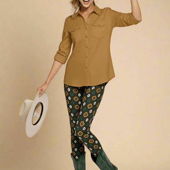 Model wearing Country Diamond Yoga Leggings with dark green base and white and yellow floral print, paired with forest green cowboy boots and a dusty mustard button-up blouse; outfit blends earthy tones with Western flair and modern activewear style.