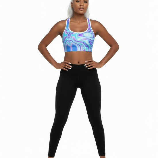 Model wearing the Dreamwave Essential Bra in a vibrant blue, purple, and white abstract pattern, paired with high‑waisted black leggings and black sneakers, standing confidently against a plain white background.