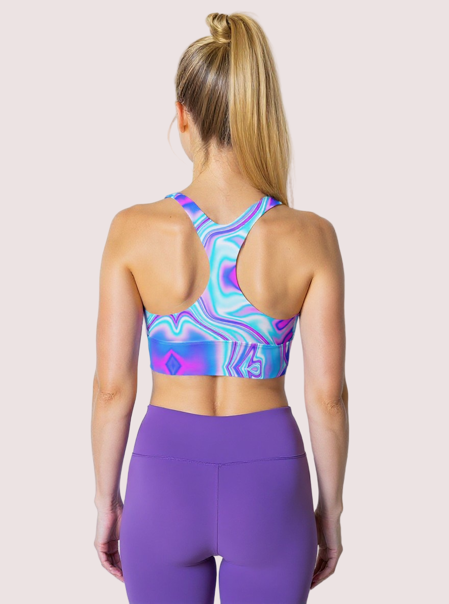 Back view of a woman wearing a "Dreamwave" longline sports bra with a swirling blue, purple, and pink pattern, paired with high-waisted purple leggings, standing against a plain background.