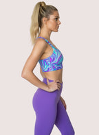 Woman wearing a colorful sports bra and purple leggings against a white background