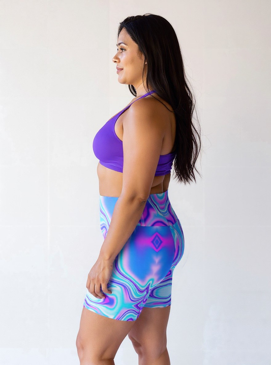 Plus-size woman in profile wearing Dreamwave Yoga Shorts featuring a vibrant blue, purple, and pink swirl pattern, paired with a purple sports bra.
