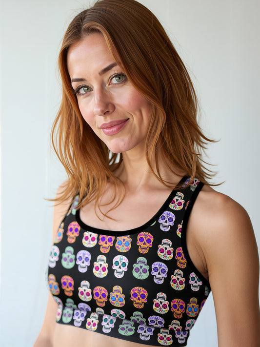 Woman wearing Eternal Bloom Essential Active Bra with a black base and colourful sugar skull print, smiling and standing against a plain background