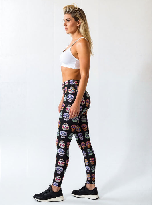 Side view of a woman wearing Eternal Bloom Yoga Leggings with a colourful skull pattern on a black background, paired with a white sports bra and black sneakers, standing against a plain background.
