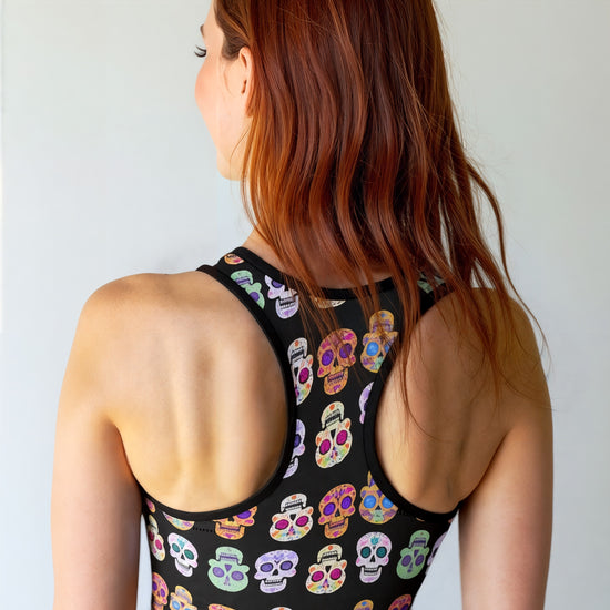 Back view of woman wearing Eternal Bloom Essential Active Bra with a black base and colourful sugar skull print, smiling and standing against a plain background