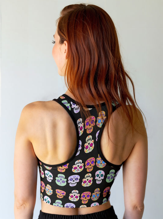 Back view of woman wearing Eternal Bloom Essential Active Bra with a black base and colourful sugar skull print, smiling and standing against a plain background