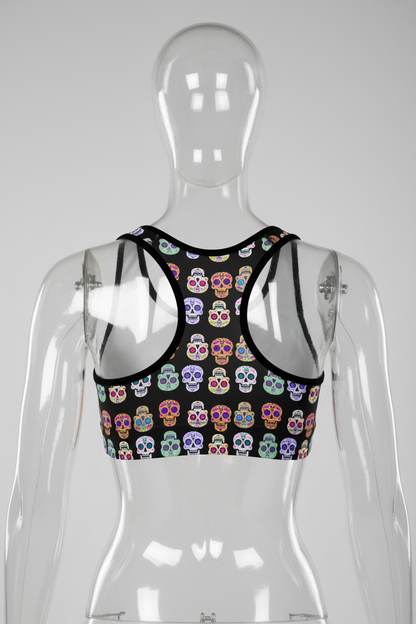 A women's racerback sports bra featuring a black base with a colorful sugar skull pattern, set against a plain white background.