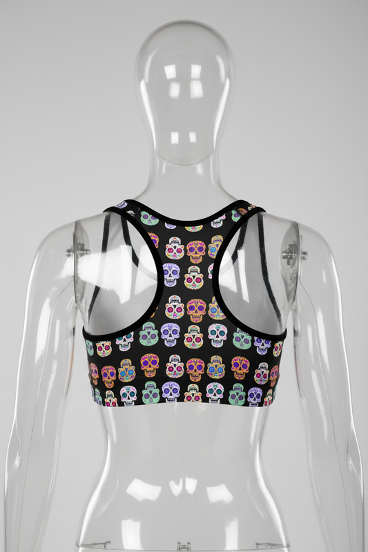 A women's racerback sports bra featuring a black base with a colorful sugar skull pattern, set against a plain white background.