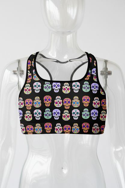 A racerback sports bra with a black background and an all-over colorful sugar skull pattern, shown against a plain white background.