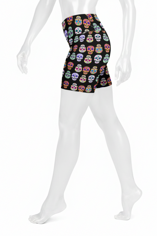 A mannequin wearing high-waisted swim trunks with a colorful sugar skull pattern on a black background, shown from the waist down against a white studio background.