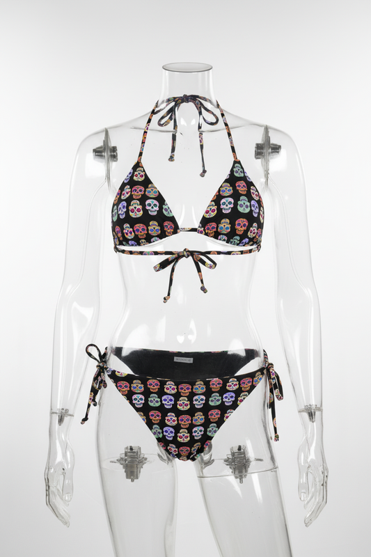 A two-piece  string bikini set featuring a black base printed with colorful sugar skull motifs, shown against a plain white background.