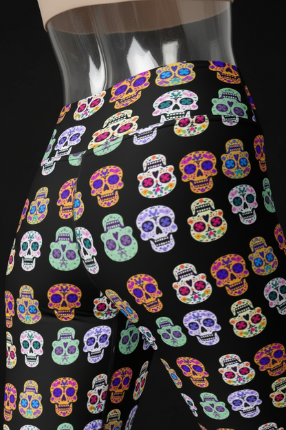 Close-up of a person wearing high-waisted black leggings with a colorful sugar skull pattern, shown from the waist to upper thigh against a white background.