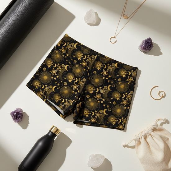 Black notebook with gold celestial pattern, black water bottle, crystal, and jewelry on a light surface