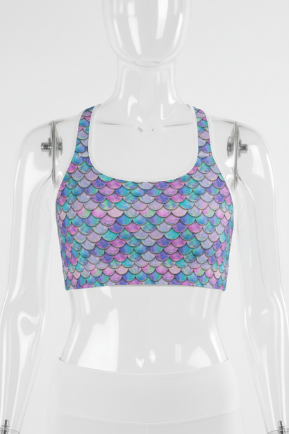 A mannequin wearing a sports bra with a colorful mermaid scale pattern in shades of purple, blue, and pink, paired with white bottoms.